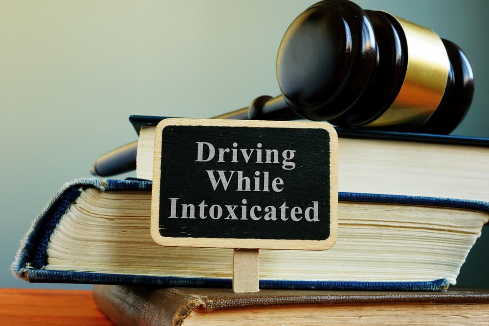 Gavel on books beside 'Driving While Intoxicated' sign.