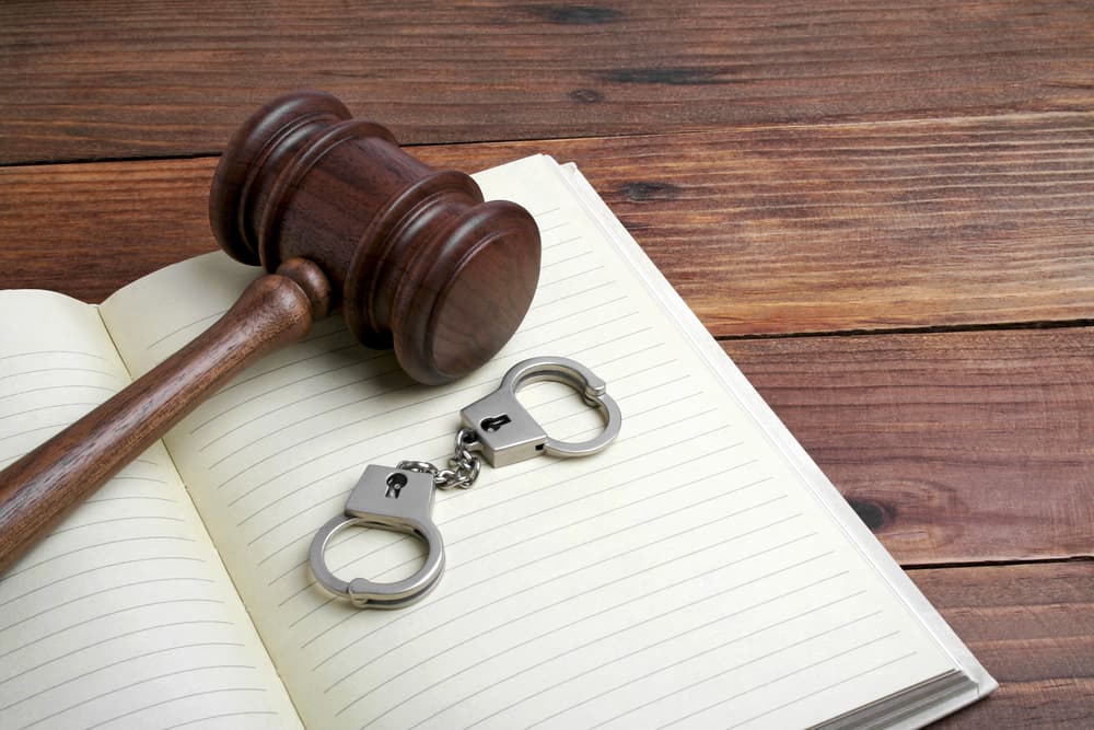 Wooden gavel and handcuffs on open notebook, symbolizing legal authority and law.