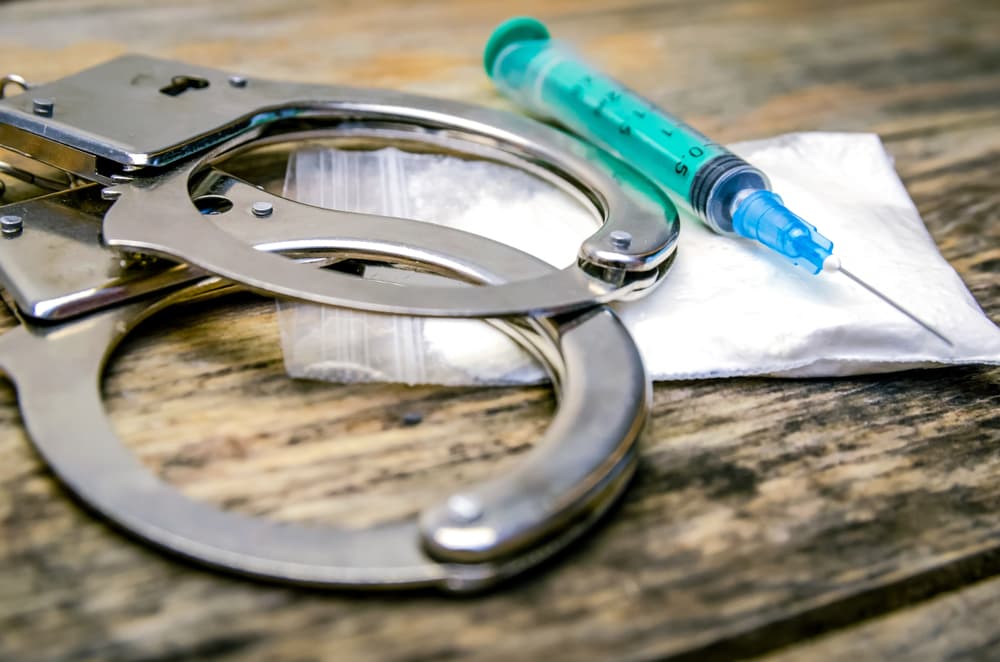Handcuffs, syringe, bag of drugs on a wooden background.