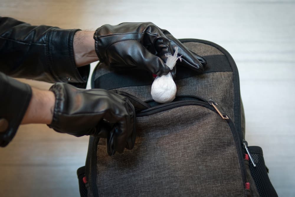 Person in gloves hiding drugs in bag, illustrating illegal drug possession scenario.