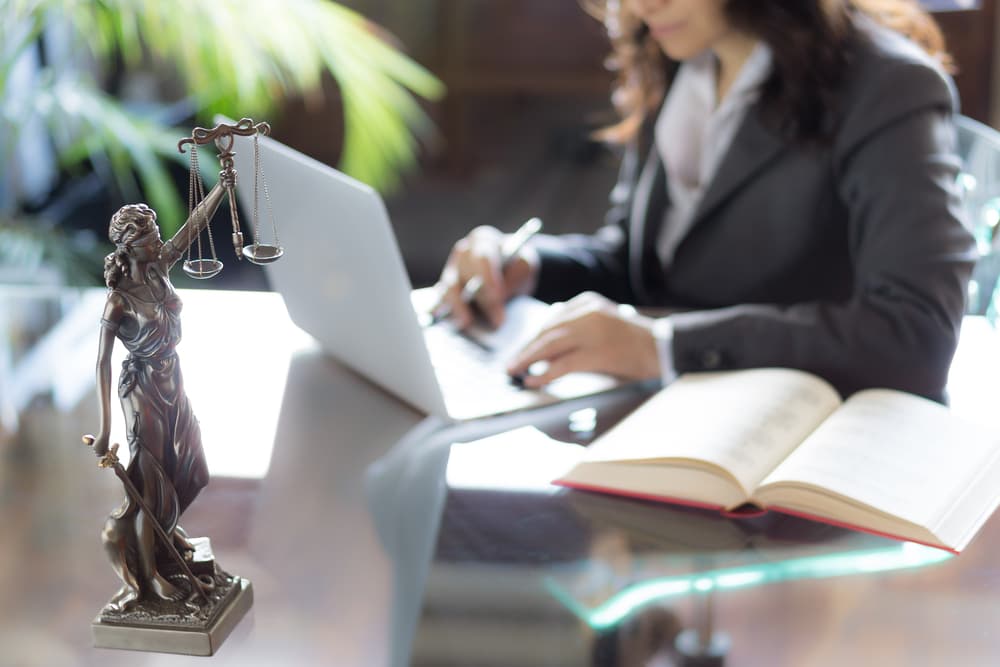 Statue of Lady Justice, lawyer working in background, symbolizing legal assistance.