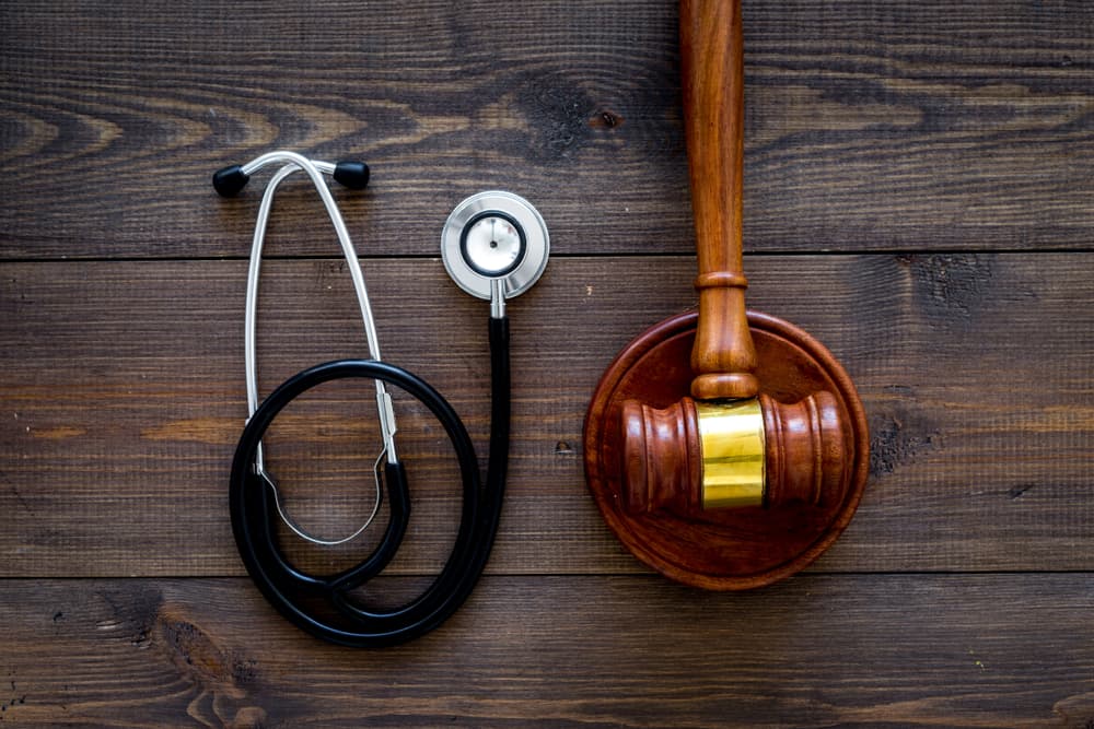 Gavel and stethoscope on dark wooden background, representing medical law and health law concept.