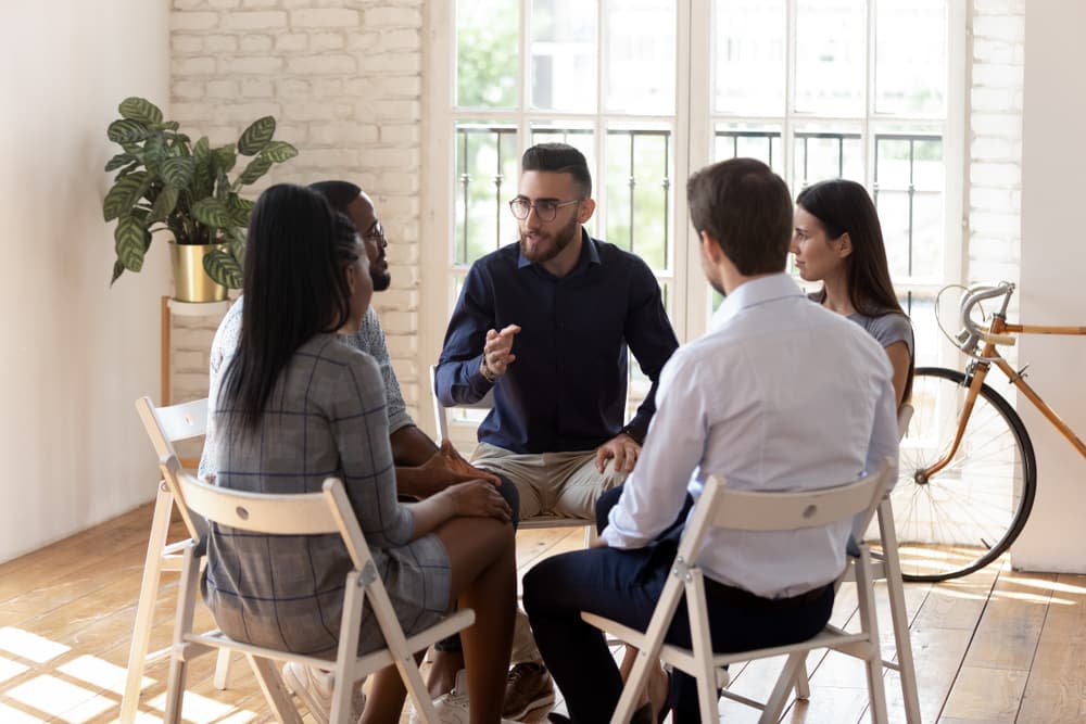 Male therapist facilitates group therapy session, supporting patients in substance addiction and mental health recovery.