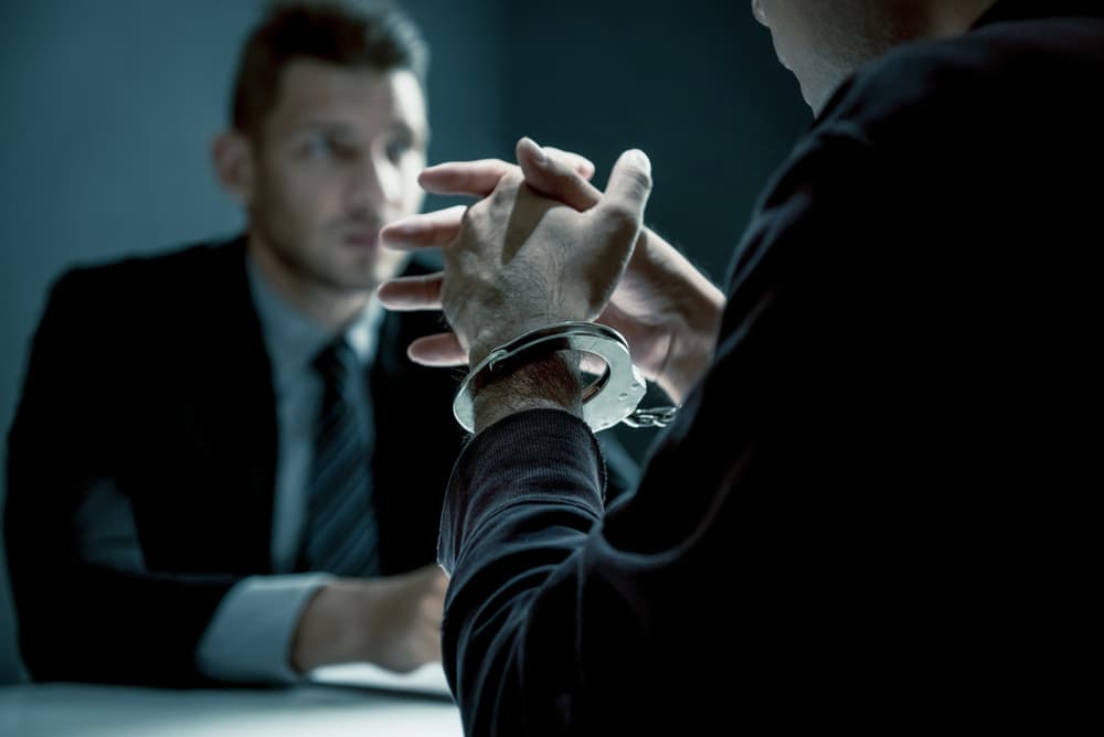 Man with handcuffs in interrogation room undergoing interview after committing a crime.
