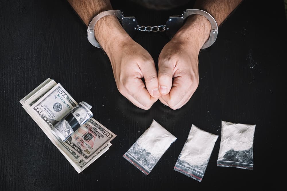 A person in handcuff with drugs in transparent bags with money