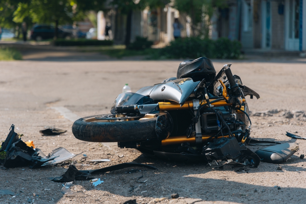 Damaged motorcycle lying on the road after a collision, with debris scattered around the crash site.